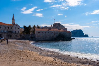Budva, Karadağ - 28 Şubat 2022: Eski Budva kasabasının plajı. Karadağ 'ın Budva kentinin antik duvarları ve kiremitli çatısı