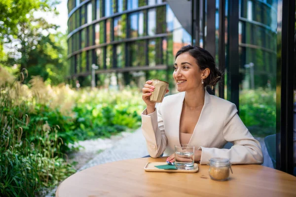 Young business woman holding and drinking coffee in street cafe in city. Portrait of beautiful woman worker waiting client on street of Prague. High quality photo