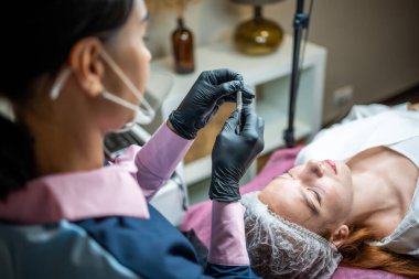 Kaş mikropatinajı prosedürü. Siyah eldivenli bir usta kaş modellerinin karışımından bir iğne yapıyor. Yüksek kalite fotoğraf