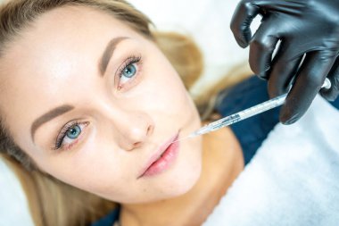 Kadının yüzünün ve elinin dudaklarının yakınında şırıngayı tutan ameliyat eldiveniyle güzellik tedavisine hazır bir şekilde çekilmiş fotoğrafı. Enjeksiyon kozmetoloji, estetik cerrahi, dudak büyütme ve düzeltme konsepti.