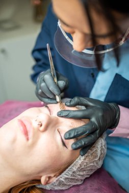 Kaş mikropatinajı prosedürü. Siyah eldivenli bir usta kaş modellerinin karışımından bir iğne yapıyor. Yüksek kalite fotoğraf