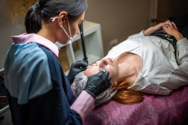 Kaş mikropatinajı prosedürü. Siyah eldivenli bir usta kaş modellerinin karışımından bir iğne yapıyor. Yüksek kalite fotoğraf