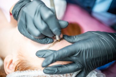 Kaş mikropatinajı prosedürü. Siyah eldivenli bir usta kaş modellerinin karışımından bir iğne yapıyor. Yüksek kalite fotoğraf