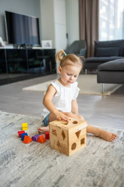 Cute caucasian little girl playing on the floor at home with eco wooden toys. Montessori toy. The child playing educational games. High quality photo