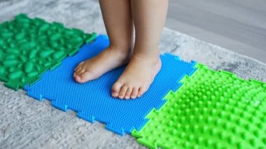 Close up view of Little girl walks on a massage mat. Toddler baby foot massage mat. Exercises for legs orthopedic massage carpet. High quality 4k footage