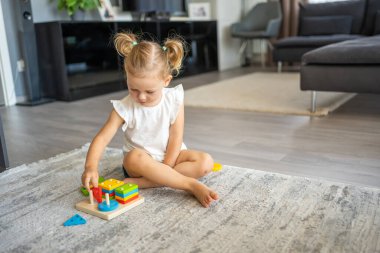 Beyaz, sevimli bir kız. Evinde yerde eko tahta oyuncaklarla oynuyor. Montessori oyuncağı. Eğitici oyunlar oynayan çocuk. Yüksek kalite fotoğraf