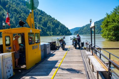  Alps, Austria - July 3, 2022: Small ferry with motorcycles on board crossing the river in the Alps mountains of Austria. High quality photo