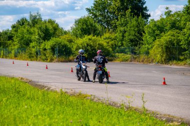 Prague, Czech Republic - July 12, 2022: Male instructor controls L-driver while she doing exercise of driving bike in skill training motordrome. Europian driver school. High quality photo