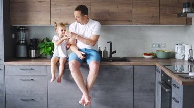 Cute little girl and her handsome dad are eating fruit in modern kitchen. Healthy eating. High quality 4k footage