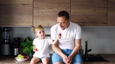 Cute little girl and her handsome dad are eating fruit in modern kitchen. Healthy eating. High quality 4k footage