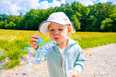 Little girl blowing soap bubbles in summer park of Prague, Czech republic. High quality photo