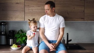 Cute little girl and her handsome dad are eating fruit in modern kitchen. Healthy eating. High quality 4k footage