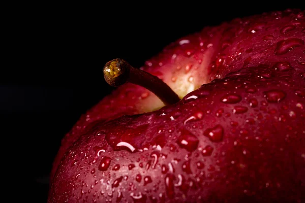 Primo piano di una mela rossa con gocce d'acqua su fondo nero. Macro foto di un frutto, umore scuro, messa a fuoco morbida — Foto Stock