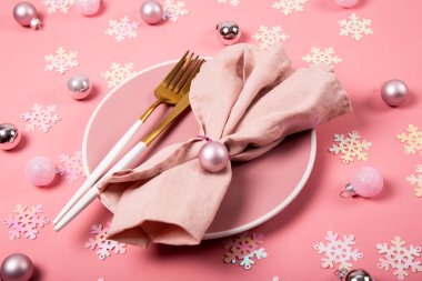 Pembe tabak, altın çatal bıçak takımı ve pembe keten peçete. Üzerinde Noel süslemeleri var. Yeni yıl tablosu kavramını pembe renkte ayarla