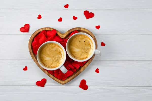 Kalp şeklinde bir tepside iki fincan kahve ve beyaz ahşap zemin üzerinde kırmızı kalpler. Sevgililer Günü için kutlama kartı. Telifsiz Stok Fotoğraflar