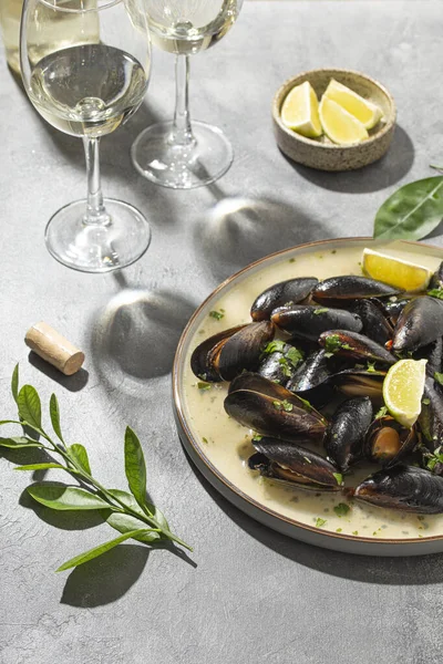 Sarımsak soslu siyah midye, otlar, limon ve yaz güneşinin altındaki masada iki bardak beyaz şarap, dikey fotoğraf.