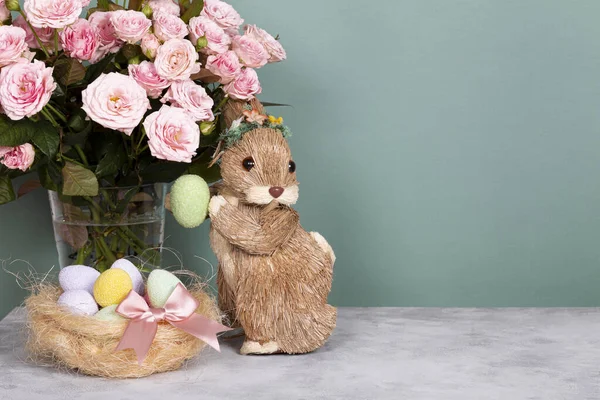 Пасхальний кролик, кольорові яйця та рожеві квіти. Святкова великодня листівка з вільним текстовим простором Стокове Фото