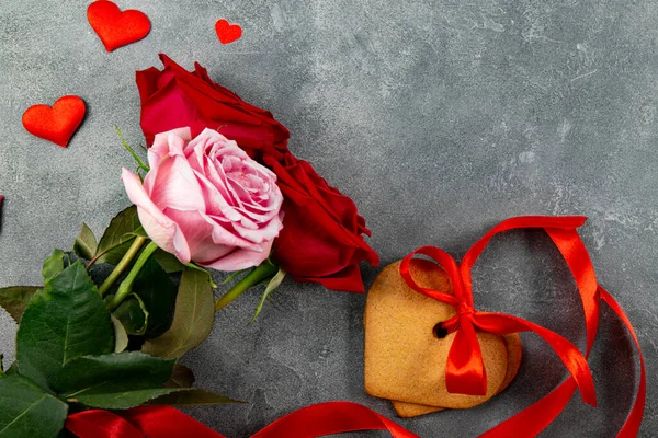 Herzförmige Kekse und ein Strauß roter und pinkfarbener Rosen auf grauem Hintergrund, Draufsicht, freier Platz für Text — Stockfoto