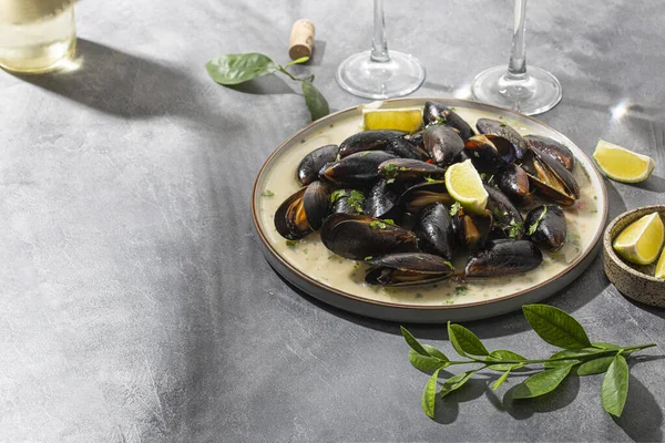 Black mussels in garlic sauce with herbs and lime and two glasses of white wine on the table under the summer sun, copy space for text - Stok İmaj