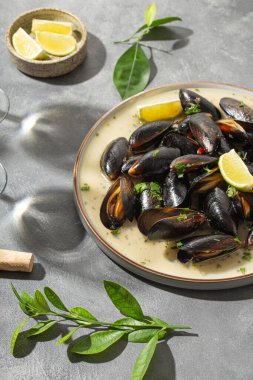 Sarımsak soslu siyah midye, otlar, limon ve yaz güneşinin altındaki masada iki bardak beyaz şarap, dikey fotoğraf.