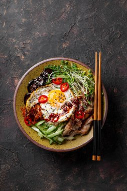 Geleneksel Kore yemeği Bibimbap. Pirinçli kase, şitake mantarı, tavuk, salatalık, mikroçerez ve Kore bibimbap sosu. Koyu arkaplan, dikey fotoğraf