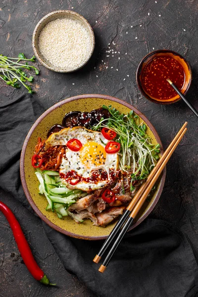 Geleneksel Kore yemeği Bibimbap. Pirinçli kase, şitake mantarı, tavuk, salatalık, mikroçerez ve Kore bibimbap sosu. Koyu arkaplan, dikey fotoğraf