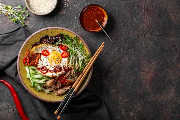 Tradiční korejské jídlo Bibimbap. Mísa s rýží, houbami shiitake, kuřecím masem, okurkou a mikrozelení a korejskou bibimbapovou omáčkou. Tmavé pozadí, kopírovat prostor pro text — Stock fotografie