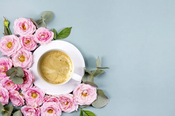 Açık mavi arka planda bir fincan kahve, pembe güller ve okaliptüs dalları. Metin için boş alanı olan güzel bir bahar kartı