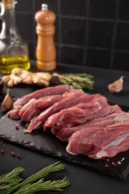 Siyah bir masanın üzerinde taze domuz eti parçaları. Dik bir siyah tahtada pişirmek için baharatlı çiğ et.