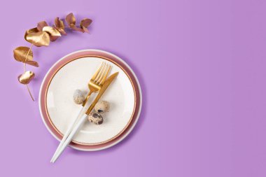  Paskalyayı kutlamak için masa ayarlayın. Tabaklar, çatal bıçak, yumurta ve altın okaliptüs dalları menekşe masa üstü görünümünde, metin alanı için kopyala