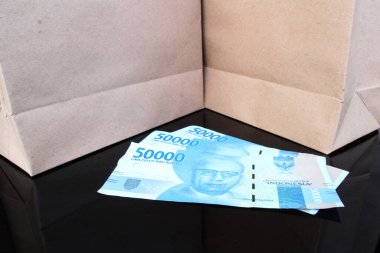 İki kahverengi kesekağıdının yanındaki siyah bir masada üç parça 50 bin rupi, alışveriş konsepti.