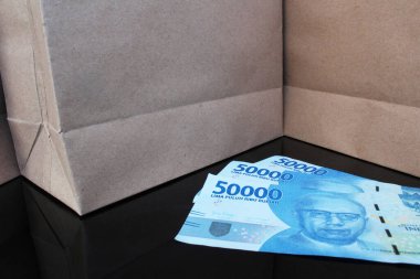 Elli bin rupia 'nın üç parçasını siyah bir masaya koy. İki kahverengi kağıt torba, Endonezya konseptinde ucuz alışveriş.