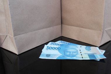 Elli bin rupiah banknot, Endonezya devlet para birimi iki kahverengi kese kağıdıyla siyah bir masa üzerinde, tutumlu alışveriş konsepti