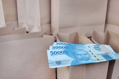 Bir sürü kese kağıdının arka planında açık kahverengi bir kese kağıdının üzerinde 50.000 rupi.