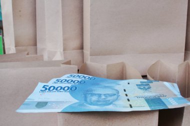 Kahverengi bir kese kağıdında, arka planda bir sürü kese kağıdı olan mavi elli bin rupiah banknotu.
