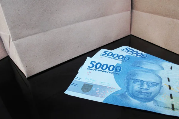 Siyah bir masanın üzerinde kağıt çantalı 350.000 rupiah banknot.