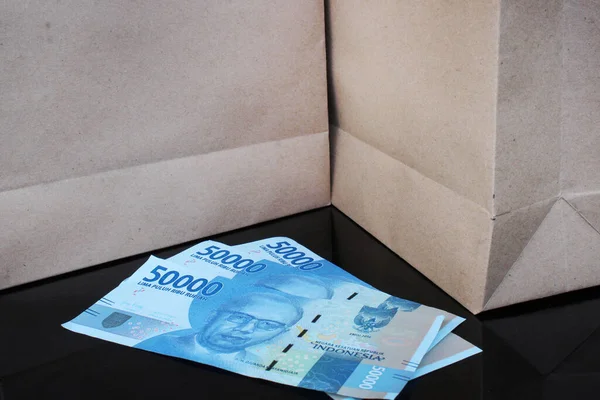 Elli bin rupiah banknot siyah bir masada kağıt torbaların arasında.