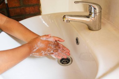 Çocuğun elleri, odasındaki krem rengi bir vajinanın üzerinde köpük olana kadar avuçlarını sabunla yıkıyor.