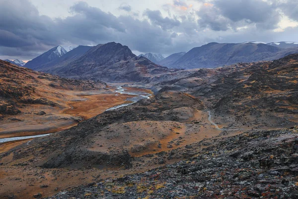 Bir nehrin arka planında dağ manzarası ve sonbaharda günbatımında fırtınalı bir gökyüzü. Altai, Rusya