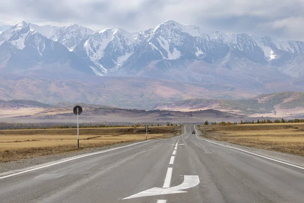 Sonbaharda bir dağ sırasının arka planındaki dağ vadisinde işaretli bir yol. Arka planda bir araba var..
