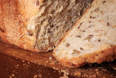 Tahta bir tahtanın üzerinde kesilmiş, tohumlu ve altın kabuklu buğday ekmeğine yakından bakın. Ev yapımı ekmek..