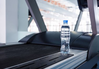Spor salonunda koşu bandında bir şişe suyla fitness konsepti.