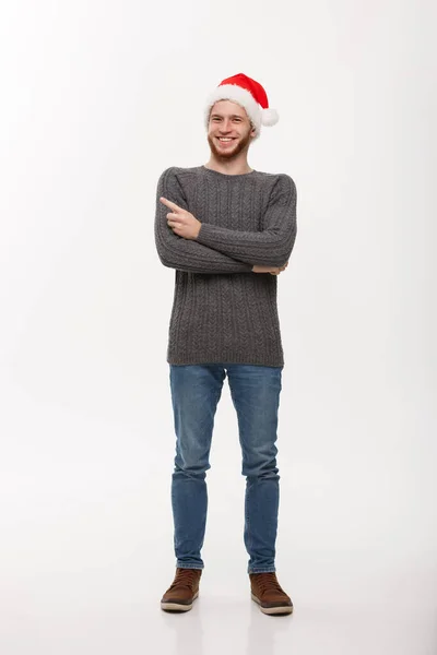 Праздник - молодой бородатый человек в свитере любит играть и показывать пальцем на бок с копирайтом. — стоковое фото