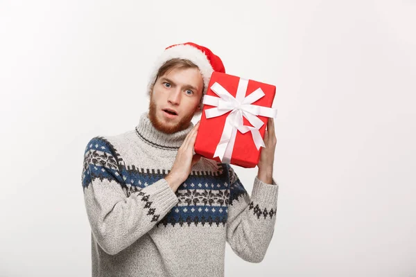 Weihnachtskonzept - fröhlicher neugieriger junger Mann mit Bart trägt Geschenk und lauscht in der Box isoliert auf weißem Hintergrund. — Stockfoto