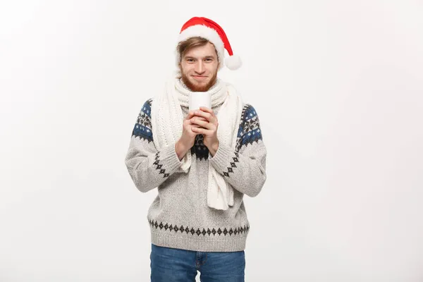 Weihnachtskonzept - junger Mann mit Bart, Pullover und Weihnachtsmütze, der eine heiße Kaffeetasse auf weiß mit Kopierraum hält. — Stockfoto