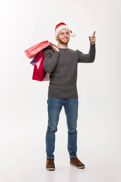 Boże Narodzenie koncepcja - atrakcyjne kaukaski młody człowiek zaskakujące, szokujące gospodarstwa torba na zakupy i wskazując palcem w przód. — Zdjęcie stockowe