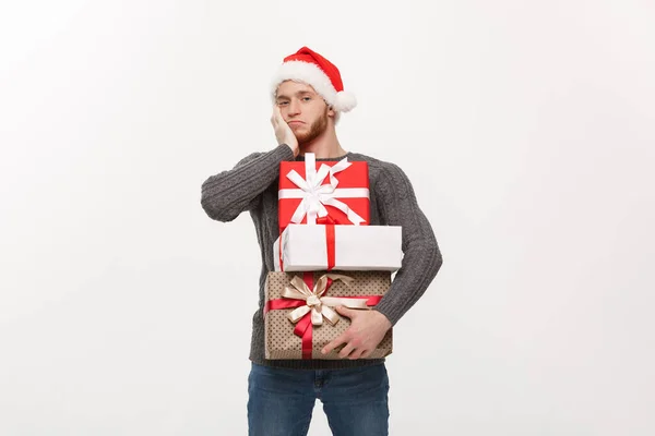 Weihnachtskonzept - junger gutaussehender Mann mit Bart und schweren Geschenken mit erschöpftem Gesichtsausdruck auf weißem Hintergrund. — Stockfoto