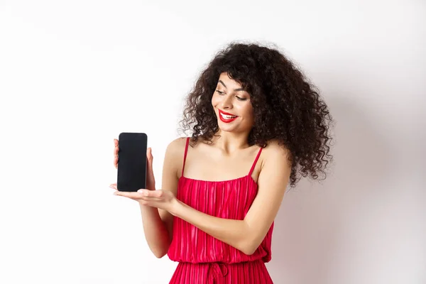 Mujer de belleza con maquillaje y cabello rizado, mostrando la pantalla vacía del teléfono inteligente, demostrar aplicación, de pie sobre fondo blanco — Foto de Stock