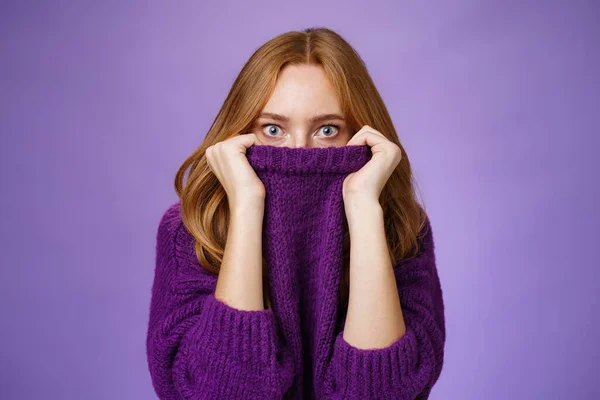 赤毛女の子怖がって冬あります来て隠れての襟の暖かいセーターポップ目ショックと唖然とでカメラで恐怖と不安立っているかのように恐れ紫色の背景 — ストック写真