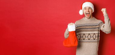 Kış tatili, yeni yıl ve kutlama kavramı. Şaşırmış ve mutlu adam sevinç çığlıkları atıyor, Noel 'in içinde hediyesini buldu çorap ve tezahürat yapıyor, elini kaldırıyor ve gülümsüyor.